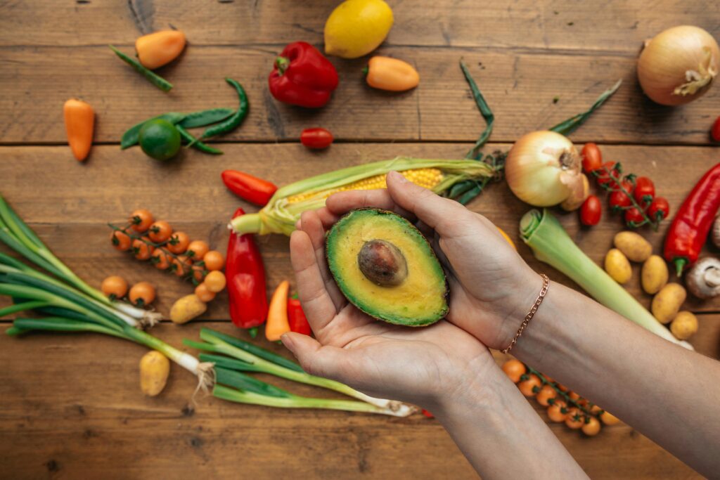 Hand holding avocado with fresh vegetables
