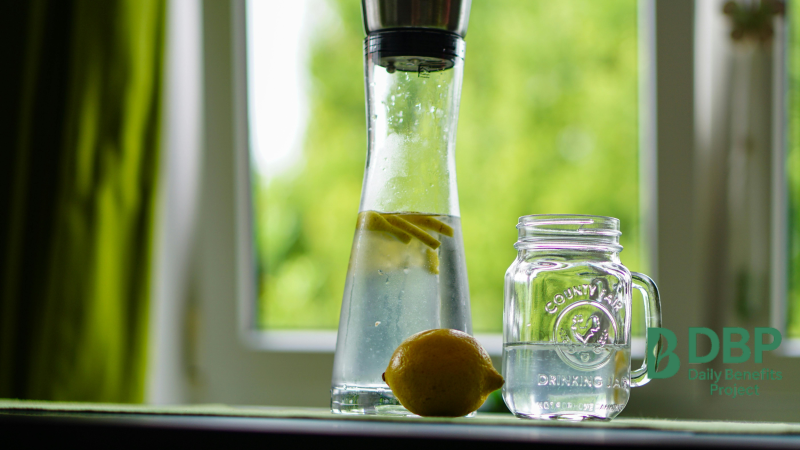 Cold or Warm Lemon Water on a Sunny Morning A glass bottle and jar with lemon water beside a lemon on a windowsill