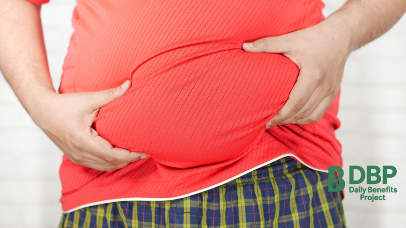 Man holding bloated stomach in red shirt Close-up of a man pressing his swollen belly with both hands