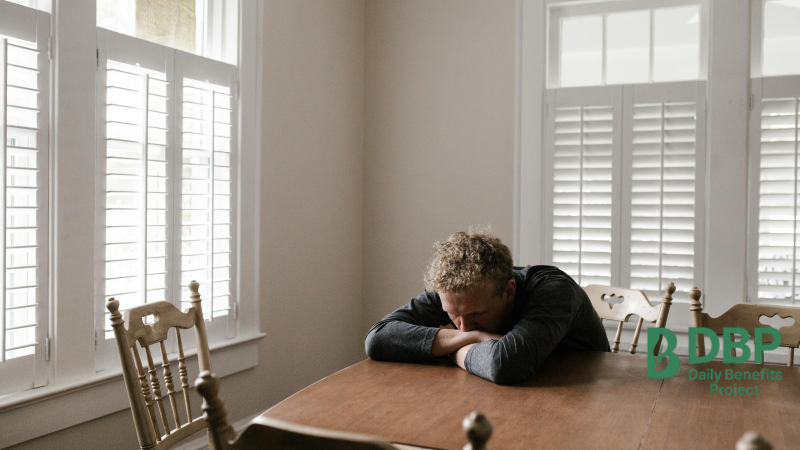 Man sitting alone with head on table feeling low Man resting his head on a dining table in a quiet, shadowy room
