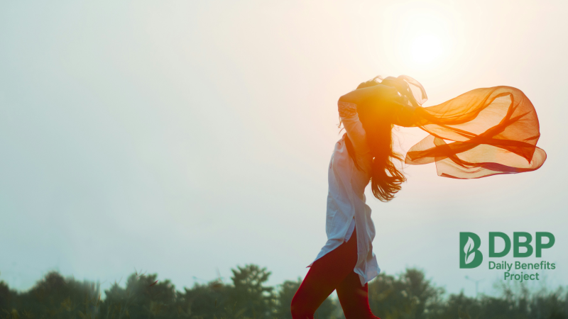 Woman enjoying freedom and sunshine in nature A woman standing in sunlight with scarf flowing behind, symbolizing wellness and energy
